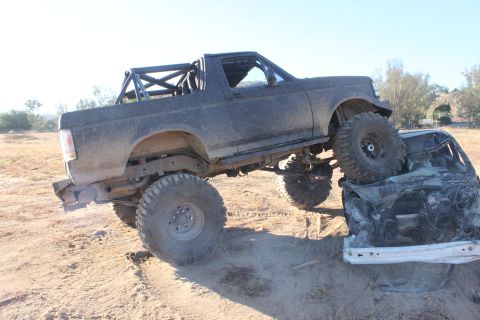 Modified 1992 Ford Bronco with roll cage on top of a crushed car