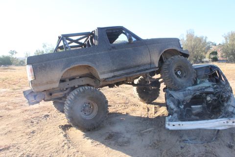 Modified SUV on top of a crushed car. The SUV has large off-road tires and a roll cage