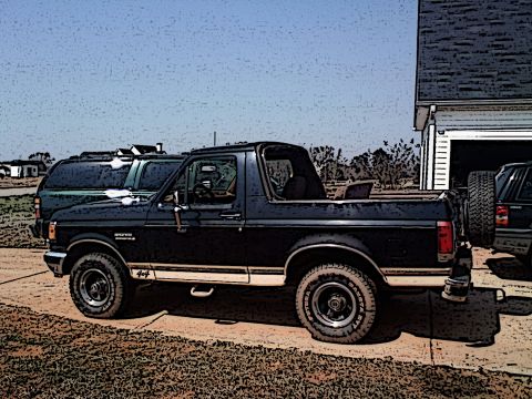 1990 Ford Bronco - A dark blue 1990 Ford Bronco is parked outside on a sunny day, with a garage and another vehicle visible in the background.