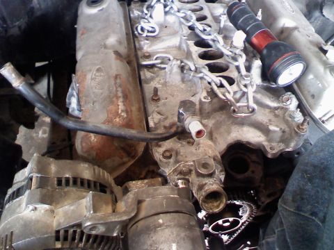 1990 Ford Bronco - Close-up of an engine bay, showing engine components and a Ford logo. A flashlight rests on a chain.