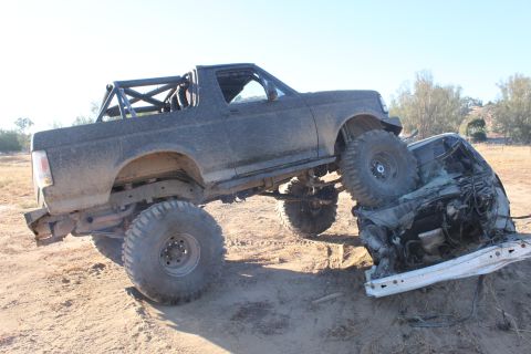 Modified 1992 Ford Bronco with roll cage on top of a crushed car
