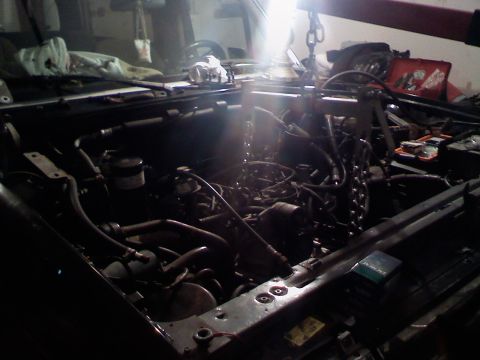 1990 Ford Bronco - The engine is suspended by chains and a hoist, ready for removal from the vehicle's engine compartment.