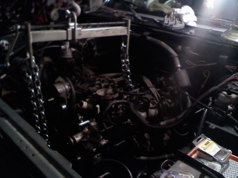 1990 Ford Bronco - Engine bay with engine hoist and chains, dark interior, some tools visible.