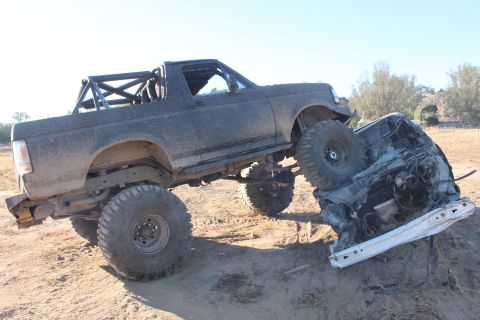 Dark gray 1992 Ford Bronco with roll cage on top of a crushed car