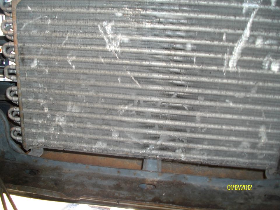 Close-up of a dirty vehicle radiator or AC condenser with visible fins and tubes