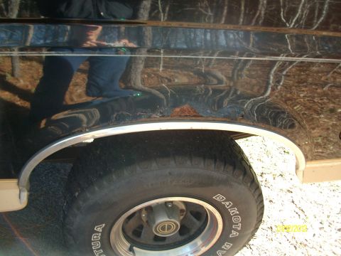 1990 Ford Bronco - Close-up of a black SUV's fender showing rust and chrome trim around the wheel well.