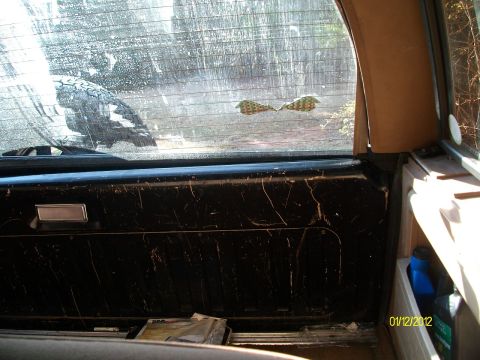 1990 Ford Bronco - View through the dirty rear window of a vehicle, showing the interior door panel.