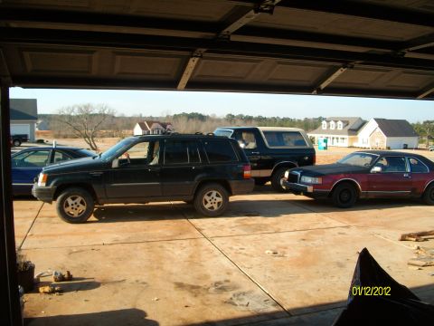 1990 Ford Bronco - Three vehicles are parked in a driveway outside a garage on a sunny day.