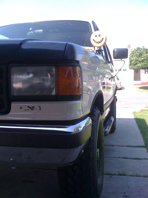 1989 Ford Bronco - The front quarter panel and headlight assembly of a white Ford F-Series truck are visible.