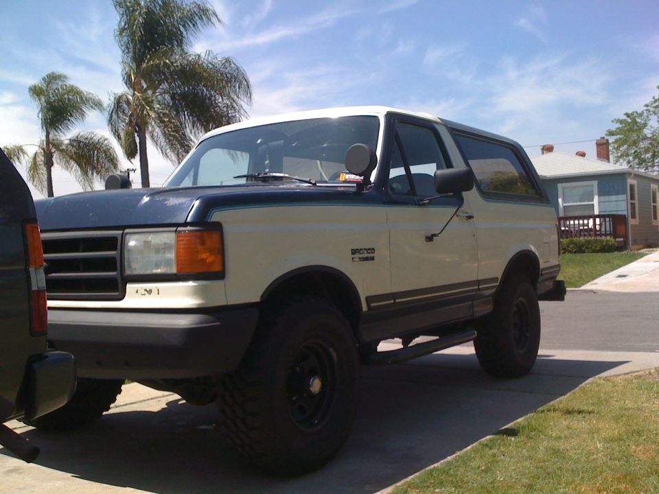 1989 Ford Bronco parked in driveway, two-tone paint, palm trees and house in background