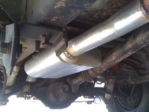 1989 Ford Bronco - The underside of a vehicle displays its exhaust system, including the muffler and drive shaft, with visible suspension parts.