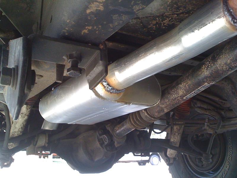 Underside view of a vehicle's exhaust pipe and muffler system, showing suspension components and rear axle