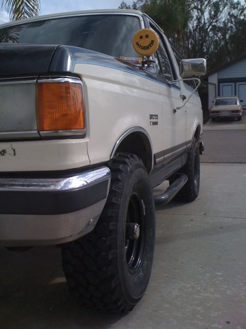 1989 Ford Bronco - This 1989 Ford Bronco is captured from a front three-quarter angle, a distinctive smiley face air freshener on the passenger side window.