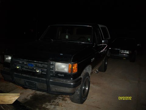 1990 Ford Bronco - A black 1990 Ford Bronco is parked outside at night, with another vehicle visible in the background.