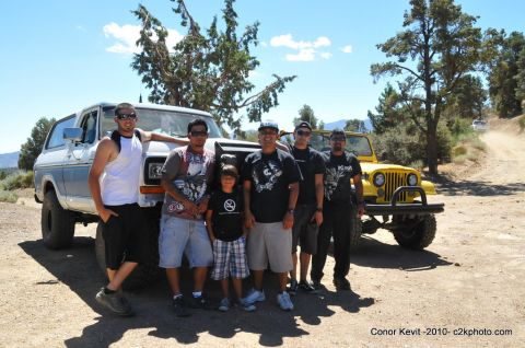 1989 Ford Bronco - A group of people stand with two off-road vehicles in a dry, wooded area under a bright blue sky.