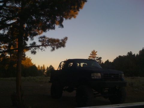 1989 Ford Bronco - Pickup truck with large tires and roll bar parked in a field during sunset.