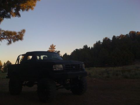 1989 Ford Bronco - A lifted pickup truck sits in a field with trees in the background under a clear sky.
