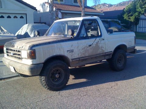 1989 Ford Bronco - A muddy Ford Bronco is parked on a residential street.