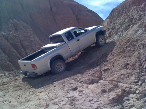 1989 Ford Bronco - A pickup truck navigates a challenging off-road trail with steep, eroded hillsides.