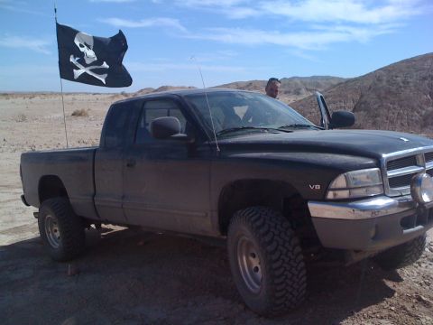 1989 Ford Bronco - A black pickup truck flies a pirate flag while parked in a desert landscape.