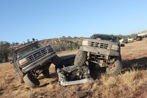 1992 Ford Bronco and another truck crushed together on a dry, grassy hill