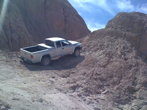 1989 Ford Bronco - Pickup truck navigating a challenging off-road path with steep, rocky hills.