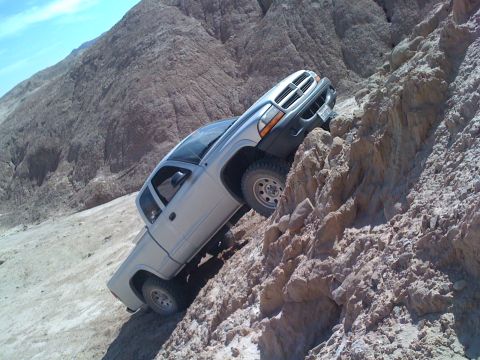 1989 Ford Bronco - Silver Dodge Dakota pickup truck navigating a challenging off-road trail on a steep, rocky incline.