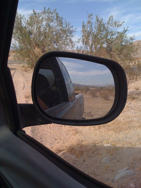 1989 Ford Bronco - Desert scenery reflected in a side view mirror, with a dirt road and sparse vegetation visible.