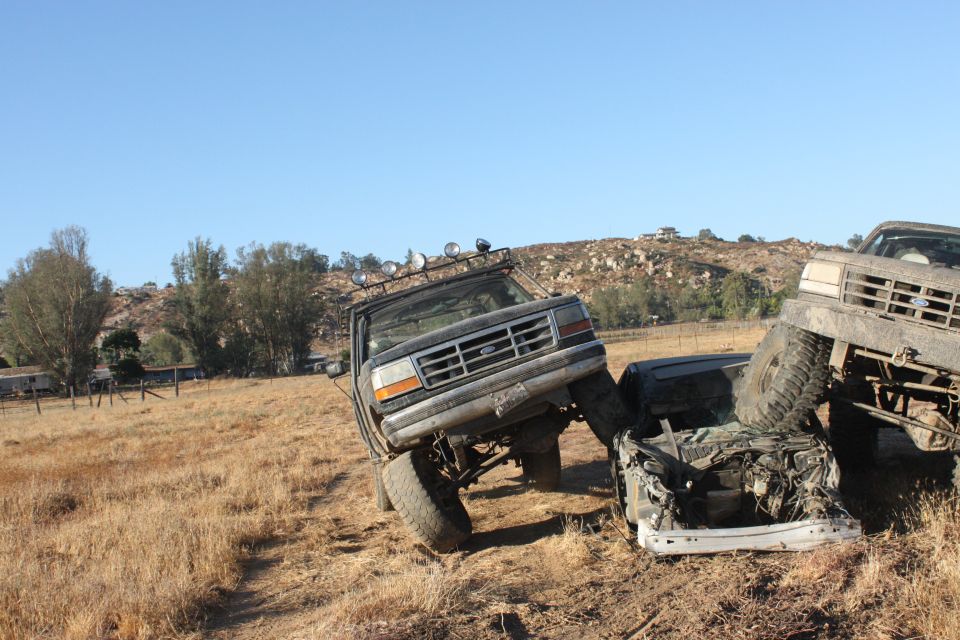 1992 Ford Bronco on its side, crushing a sedan, with another truck behind