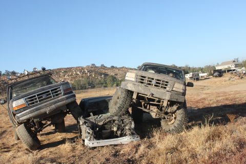 1992 Ford Bronco and another truck off-road, one crushing a car