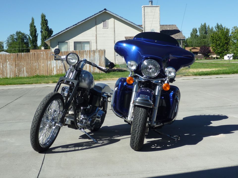 Blue touring motorcycle with batwing fairing beside gray custom bobber on driveway