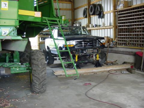 1992 Ford Bronco - A dark Ford Bronco with a white top sits up on yellow jack stands inside a metal pole barn, its front bumper removed to expose the frame ho…