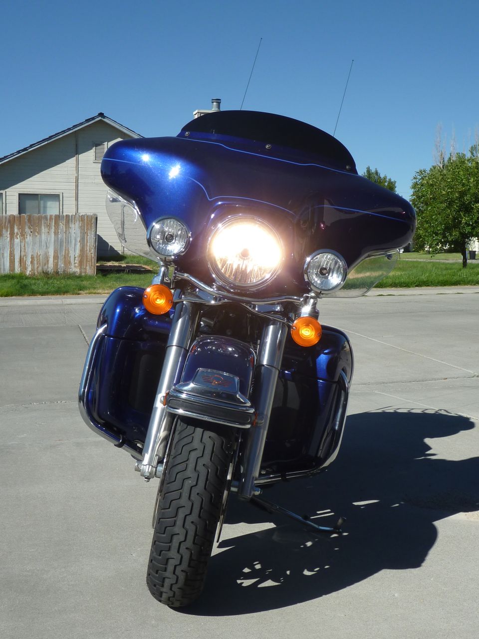 Front view of a blue motorcycle parked on pavement, with a house and fence in the background
