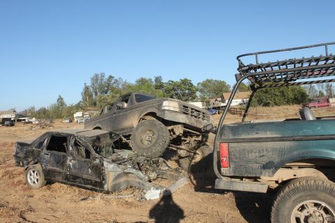 Muddy trucks piled on top of a crushed car in a junkyard