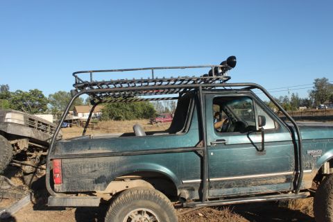 Green Ford Bronco with roll cage and roof rack, another vehicle in front