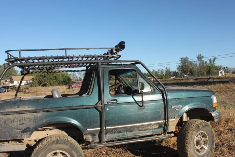 Green 1992 Ford Bronco with a custom roof rack and roll cage, seen from the side at a three-quarter front angl