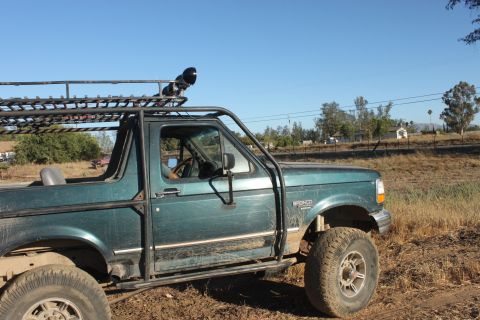 Green 1992 Ford Bronco with roof rack and off-road tires parked in a dry, grassy field