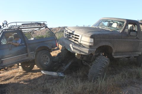 Muddy Ford Bronco stuck against another off-road vehicle on a hill