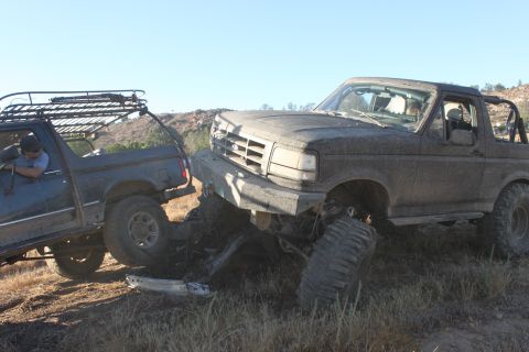 Mud-covered 1992 Ford Bronco with a damaged front bumper, stuck next to another off-road vehicle