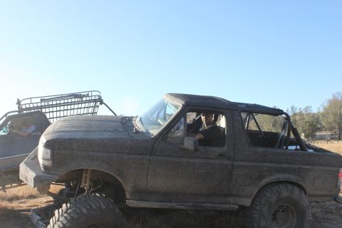 Muddy SUV with a roll cage and large tires, driver visible. Another vehicle with a rack is behind it