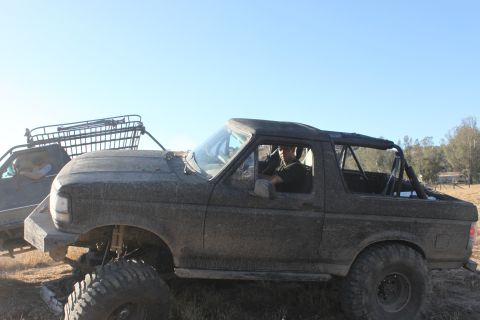 Mud-covered 1992 Ford Bronco with a roll cage, lifted suspension, and off-road tires, seen from the 3/4 front