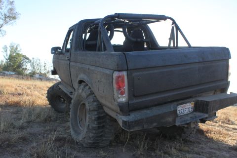 Modified Ford Bronco with roll cage and large tires, parked off-road