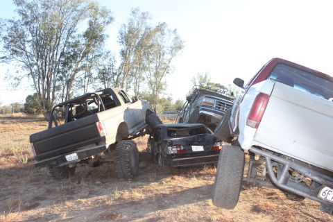 1992 Ford Bronco, lifted and modified, is partially crushed by other off-road vehicles in a junkyard scene