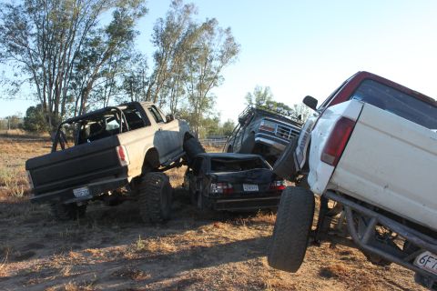 1992 Ford Bronco on top of a crushed car, with other modified trucks