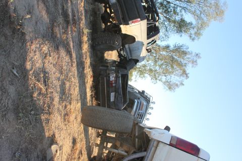 Several off-road vehicles overturned on dirt ground with trees and clear sky in background. Supermotors.net lo