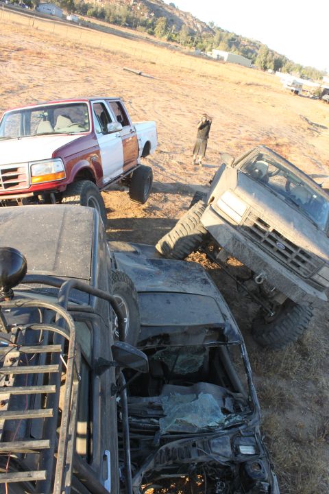1992 Ford Bronco, red and white, lifted, with large tires, parked next to other off-road vehicles