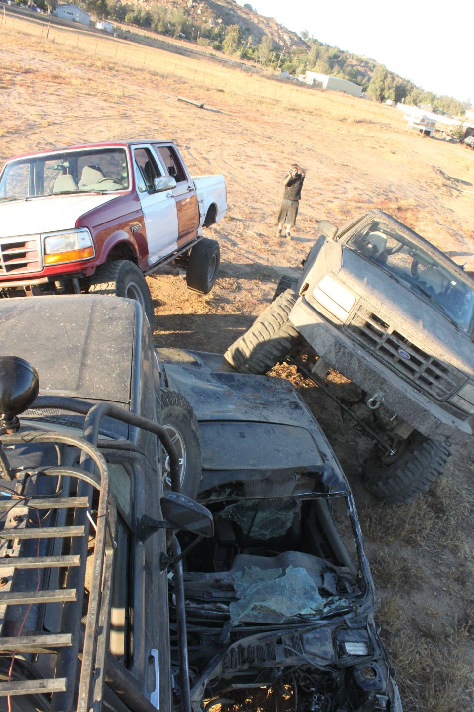 1992 Ford Bronco, red and white, lifted, with large tires, parked next to other off-road vehicles