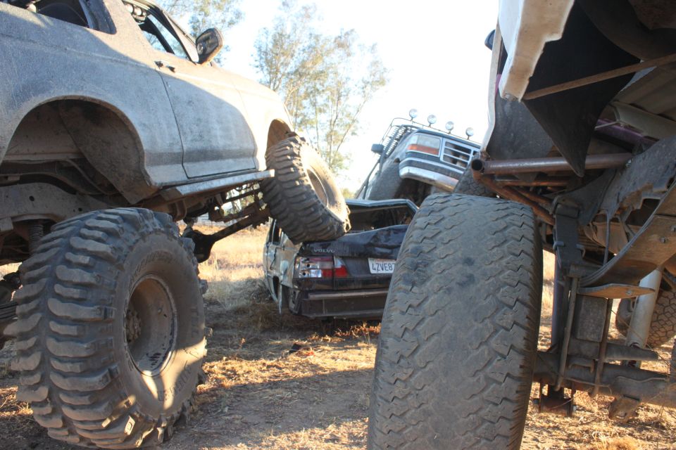 Mud-splattered truck with large tires, another vehicle on top, and a car in between