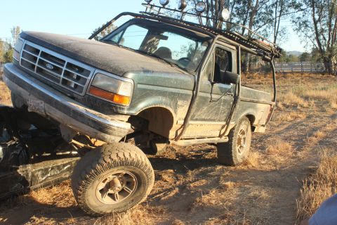 Green pickup truck with off-road lights and roll cage, front-left tire on another vehicle