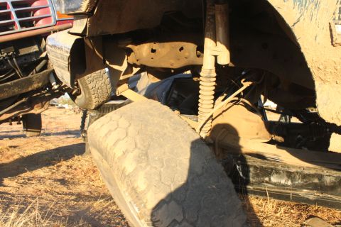 Undercarriage view of a muddy truck with a tire in the foreground. Another vehicle is partially visible on the